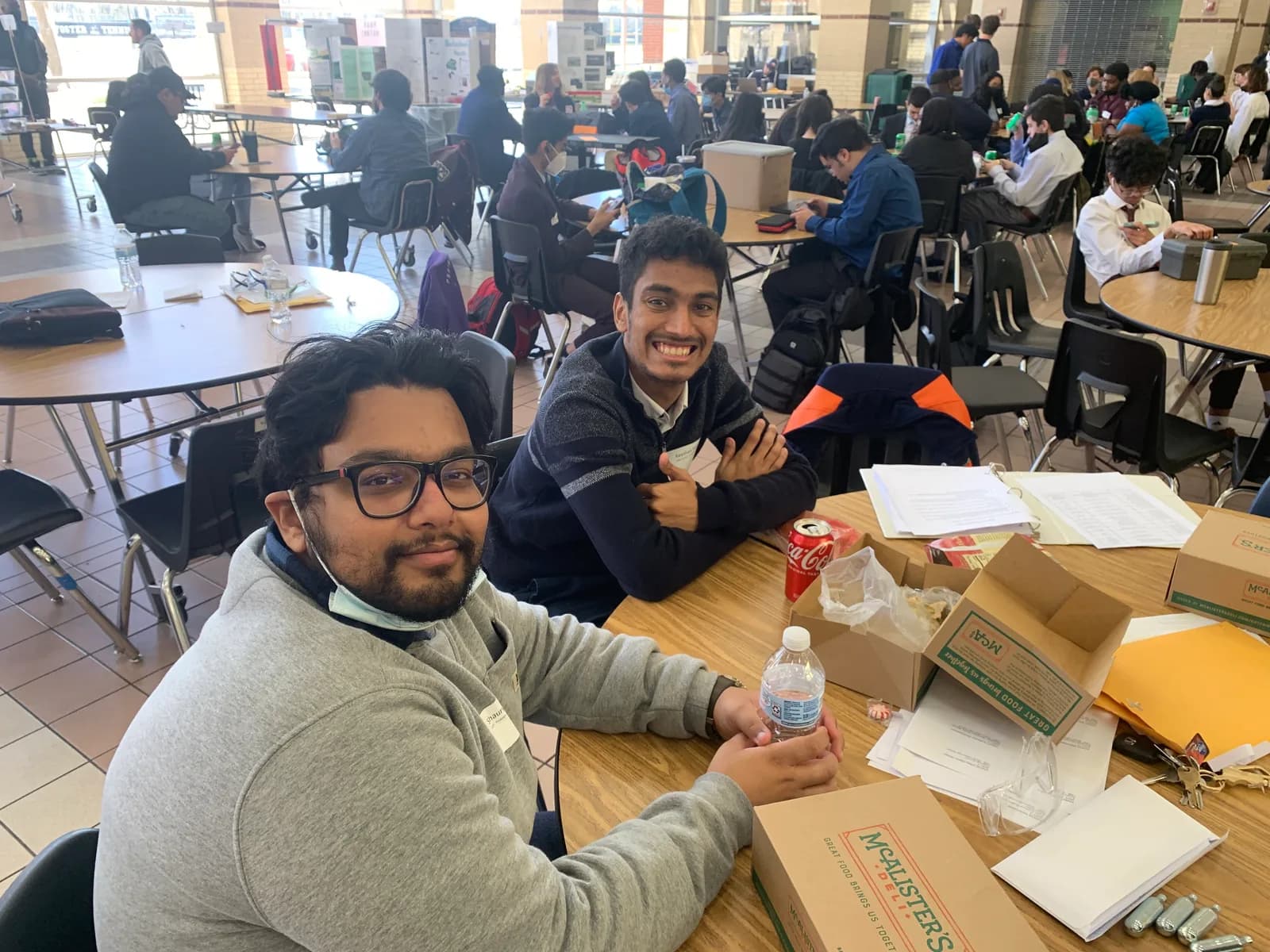 Two members smiling over competition kits and boxes in the cafeteria
