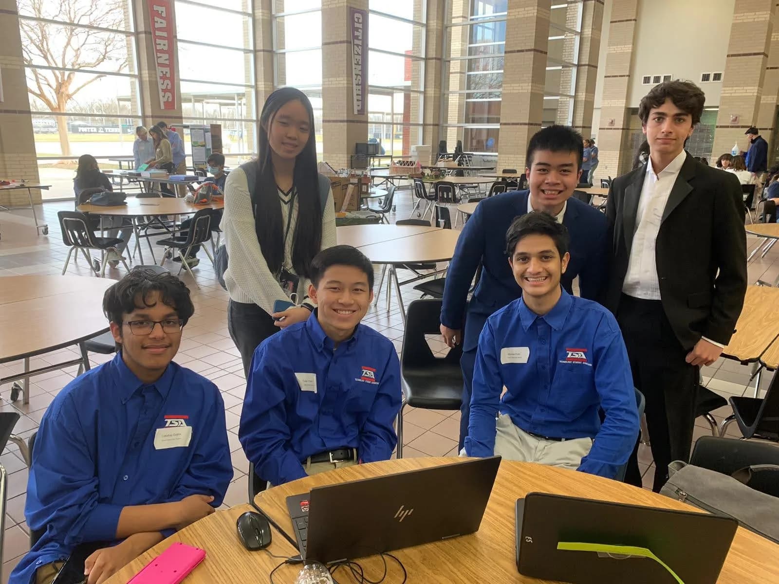 Six members posing together at a work table